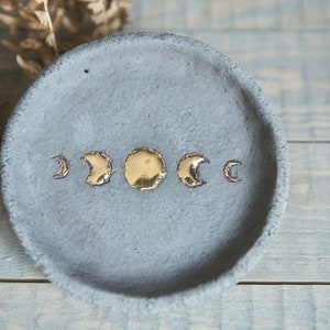 以下が含まれることがあります： 金色の月相のデザインが施された灰色のセラミック製の皿。ジュエリー、鍵、その他の小さなアイテムを収納するのに最適です。