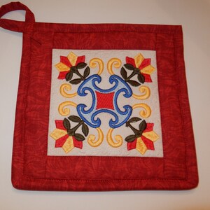 May include: Red and white quilted pot holder with a floral design featuring yellow, red, blue, and green embroidery.