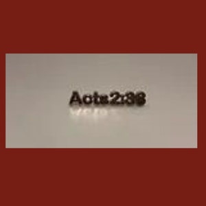 Op de afbeelding: Een close-up van een klein, zilverkleurig metalen label met de tekst "Handelingen 2:38" erop gegraveerd.