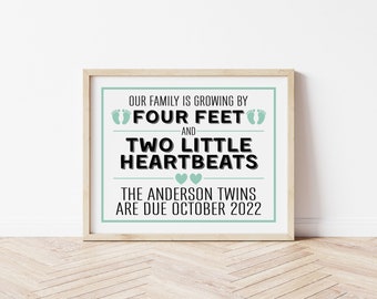 May include: A framed print with the text "OUR FAMILY IS GROWING BY FOUR FEET AND TWO LITTLE HEARTBEATS." The text also reads "THE ANDERSON TWINS ARE DUE OCTOBER 2022." The print has a light green border and is in a wooden frame.