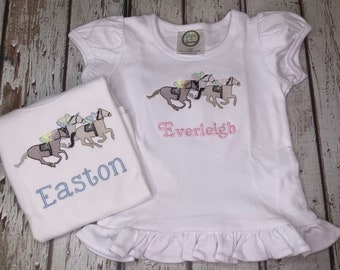 Puede incluir: Dos camisetas blancas con imágenes bordadas de caballos y jinetes. La camiseta de arriba tiene el nombre "Everleigh" bordado en rosa. La camiseta de abajo tiene el nombre "Easton" bordado en azul.