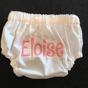 Op de afbeelding: Witte babybloomers met elastische taille en beenopeningen. De naam "Eloise" is roze op de voorkant geborduurd. De bloomer is gemaakt van een zachte, lichte stof.