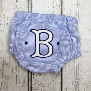 Op de afbeelding: Baby bloomer in blauw en wit ruitpatroon, met een elastische tailleband. De bloomer heeft een grote, wit geborduurde letter "B" met een marineblauwe omtrek en twee marineblauwe stippen.