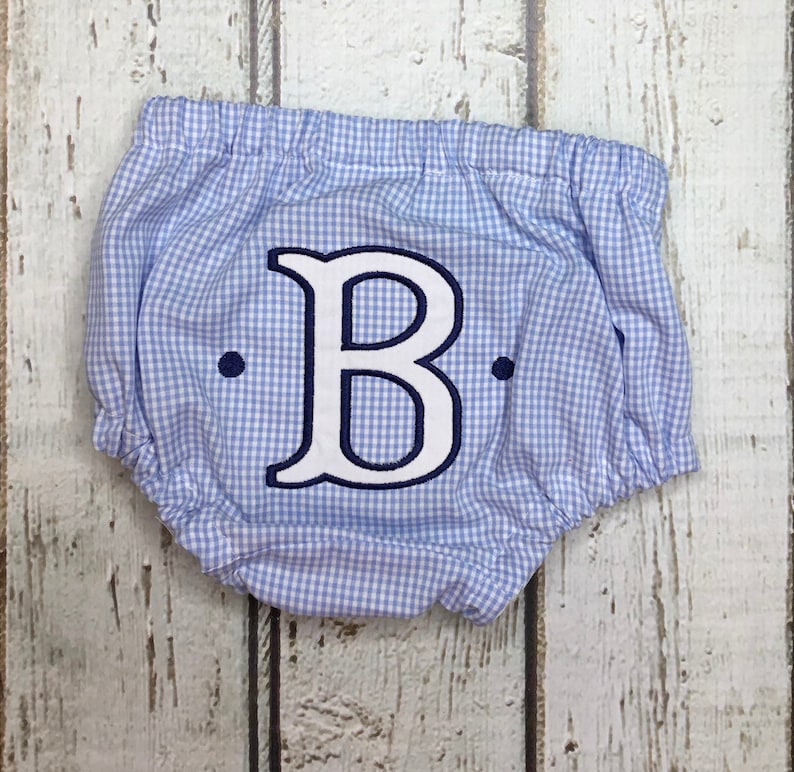 Op de afbeelding: Baby bloomer in blauw en wit ruitpatroon, met een elastische tailleband. De bloomer heeft een grote, wit geborduurde letter "B" met een marineblauwe omtrek en twee marineblauwe stippen.