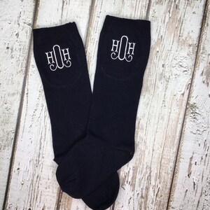 K&ouml;nnte beinhalten: Ein Paar schwarze Kniestr&uuml;mpfe mit wei&szlig;en gestickten Initialen "HOH" auf jeder Strumpf.