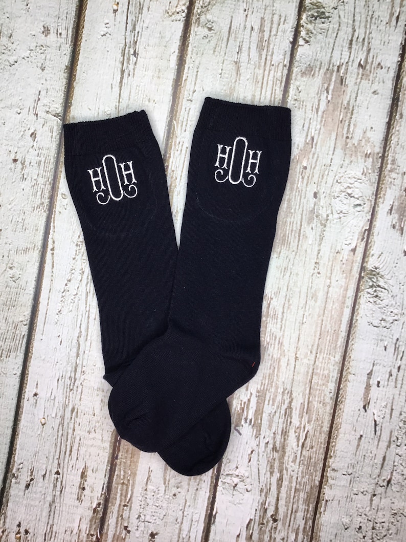 K&ouml;nnte beinhalten: Ein Paar schwarze Kniestr&uuml;mpfe mit wei&szlig;en gestickten Initialen "HOH" auf jeder Strumpf.