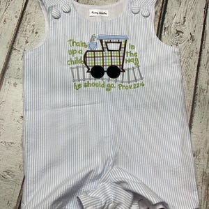 May include: A blue and white striped baby romper with a train applique and the text "Train up a child in the way he should go. Prov. 22:6".