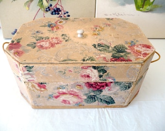 May include: A vintage, two-tiered, octagonal storage box with a floral pattern and a white knob on the lid. The box is made of cardboard and has a floral design with pink, red, and green colours.
