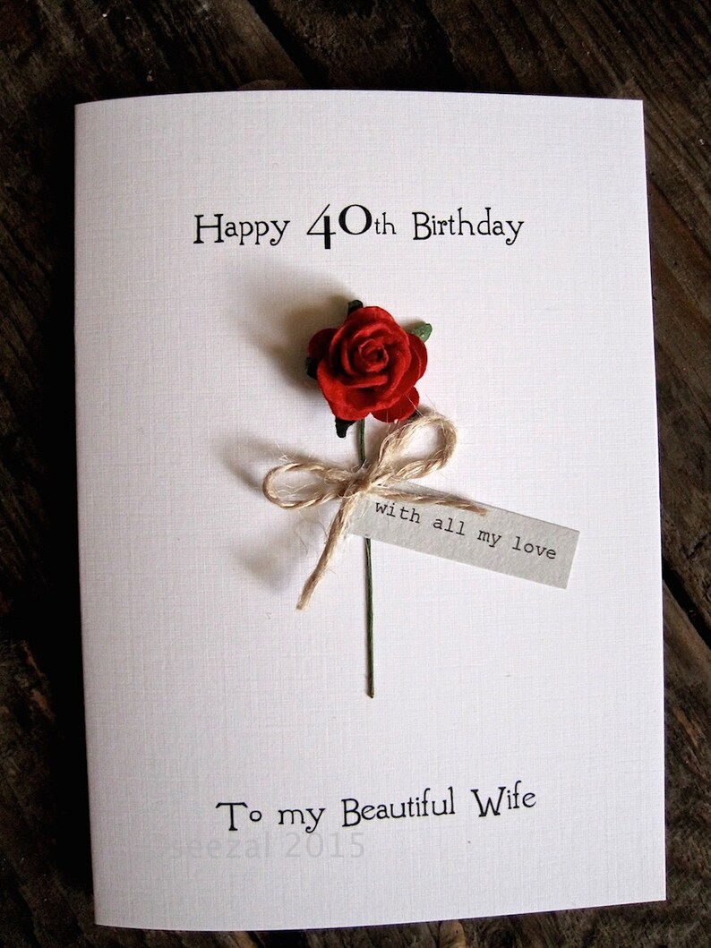 May include: A white birthday card with the text "Happy 40th Birthday" and "To my Beautiful Wife." A red rose with a twine bow and a tag that reads "with all my love" is attached to the card.
