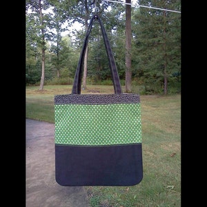 May include: A black and green tote bag with a black strap. The bag has a green patterned fabric with a black bottom.
