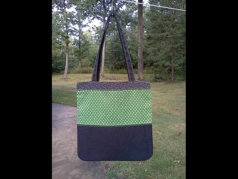 May include: A black and green tote bag with a black strap. The bag has a green patterned fabric with a black bottom.