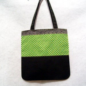 May include: A black and green tote bag with a white polka dot pattern. The bag has two black straps and a black bottom.