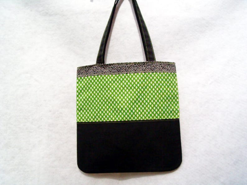 May include: A black and green tote bag with a white polka dot pattern. The bag has two black straps and a black bottom.