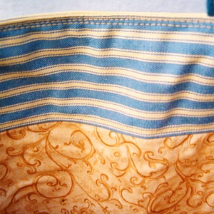 May include: Close-up of a blue and white striped fabric with a brown and white patterned fabric underneath. The striped fabric has a stitched seam along the top edge.