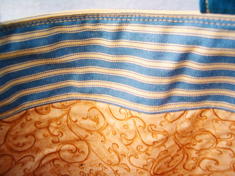 May include: Close-up of a blue and white striped fabric with a brown and white patterned fabric underneath. The striped fabric has a stitched seam along the top edge.