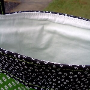 May include: A black and white fabric bag with a green fabric lining. The bag has a white polka dot pattern on the black fabric and a green floral pattern on the green fabric.
