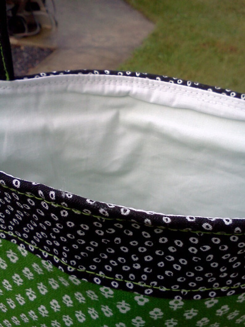 May include: A black and white fabric bag with a green fabric lining. The bag has a white polka dot pattern on the black fabric and a green floral pattern on the green fabric.