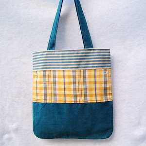 May include: A blue tote bag with a striped fabric top, a plaid fabric middle section, and a solid blue fabric bottom.