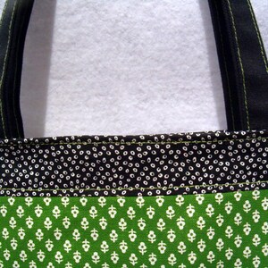May include: A black and green tote bag with a white polka dot pattern on the top section and a smaller white floral pattern on the bottom section. The bag has black straps with green stitching.