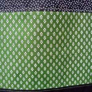 May include: A green tote bag with a white floral pattern. The bag has a black fabric lining and a black handle.