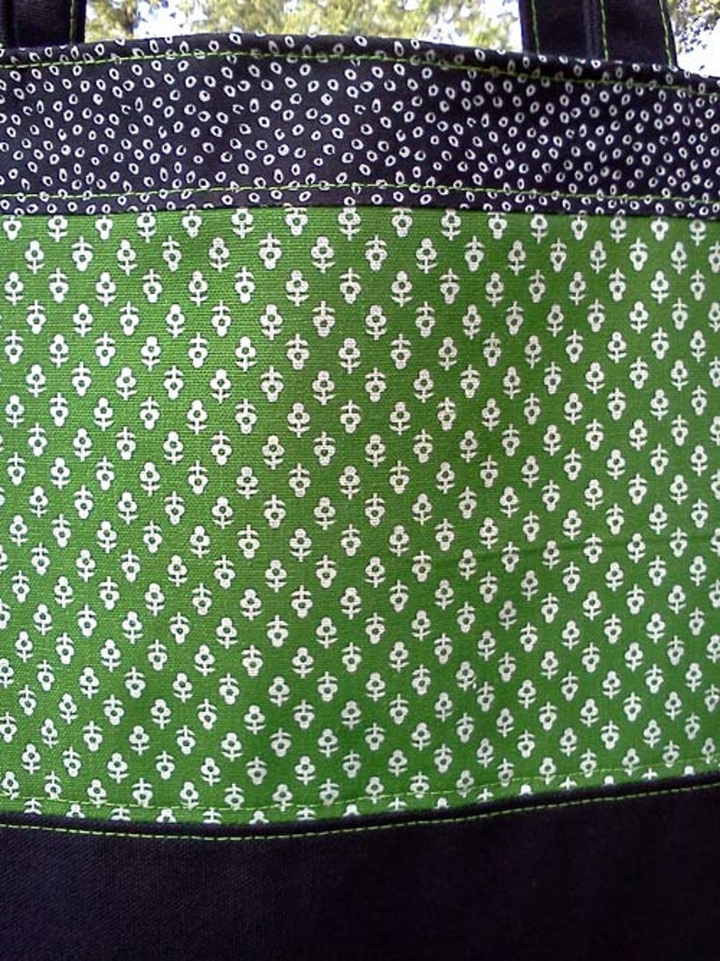 May include: A green tote bag with a white floral pattern. The bag has a black fabric lining and a black handle.