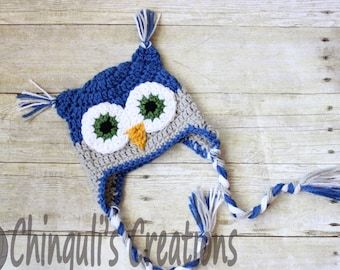 May include: Blue and gray crocheted owl hat with white and blue tassels. The hat has a long, braided tie with white and blue stripes.