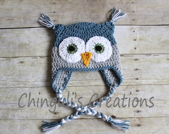 May include: A crocheted owl hat with blue, gray, white, and orange yarn. The hat has a long braided tie with tassels.