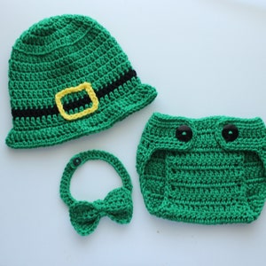 May include: A green crocheted hat with a black and yellow belt, a green crocheted nappy with black buttons, and a green crocheted bow tie.