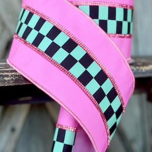 May include: A roll of wide ribbon featuring a vibrant pink base color with a central horizontal band of black and mint green checkered pattern. The edges of the checkered section are lined with thin, shimmering pink metallic glitter trim.