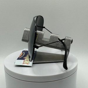 May include: Black sunglasses with a metal frame and black arms. The sunglasses are displayed on a silver stand with a white base.