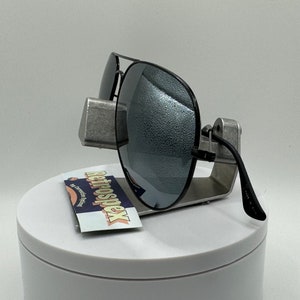 May include: Black aviator sunglasses with mirrored lenses on a silver display stand. The sunglasses have a black frame and are made in China.