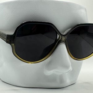 May include: A pair of large, round, brown sunglasses with dark lenses. The sunglasses have a gold trim around the lenses.