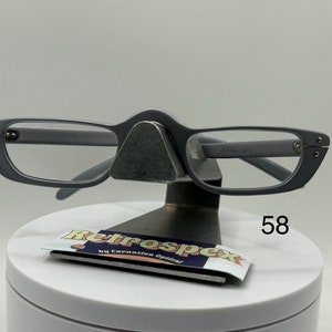 May include: Gray reading glasses with a retro style frame. The glasses are on a display stand with a label that says "RetroSpex by Carnation Optical" and the number "58".