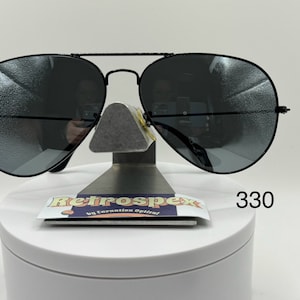 May include: Black aviator sunglasses with dark gray lenses. The sunglasses are on a white display stand with a black label that says "Retrospec by Carnation Optical" and the number "330".