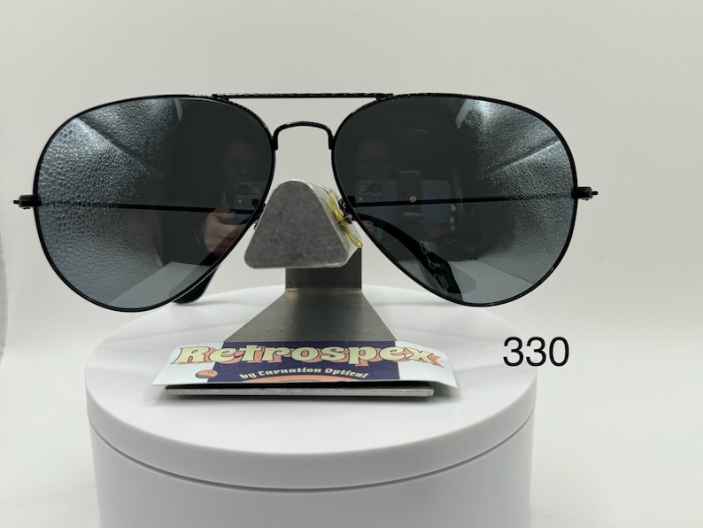 May include: Black aviator sunglasses with dark gray lenses. The sunglasses are on a white display stand with a black label that says "Retrospec by Carnation Optical" and the number "330".