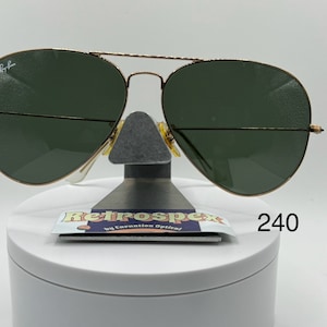 May include: Gold aviator sunglasses with green lenses. The sunglasses are on a white display stand with a label that reads "Retrospec by Convention Optical!" and the number "240".