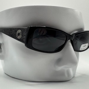 May include: Black sunglasses with a patterned frame and polarized lenses. The sunglasses have a silver circle detail on the frame.