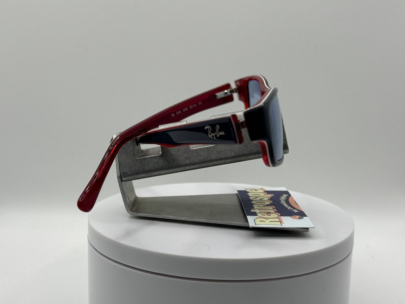 May include: Red and blue sunglasses with silver accents. The sunglasses are on a display stand with a business card that says "Retrospecs" on it.