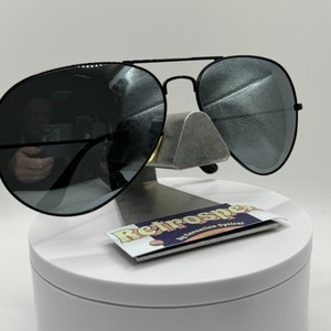 May include: Black aviator sunglasses with mirrored lenses. The sunglasses are on a white display stand with a business card that says "Retrospec by Salvation Optician".