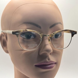 May include: Eyeglasses with a brown and tan marbled pattern on the upper frame and temples. The lower frame is a thin, gold-colored metal. The lenses are clear. The glasses are displayed on a mannequin head.