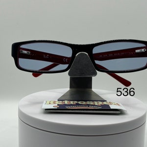 May include: Black rectangular eyeglasses with red frames and blue tinted lenses. The glasses are on a display stand with a white base and a black metal stand. The number 536 is printed on the base of the stand.