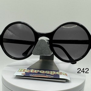 May include: Black round sunglasses with a black frame and gray lenses. The sunglasses are on a white stand with a label that says "Retrospec by Expansion Optical" and "242".