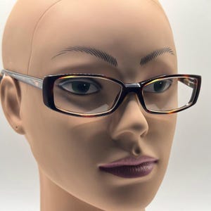 May include: Rectangular eyeglasses with a brown tortoiseshell pattern on the frames. The temples are a silver color. The glasses are on a mannequin head.