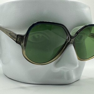 May include: A pair of vintage sunglasses with a dark gray frame and green lenses. The sunglasses have a rounded, oversized shape.