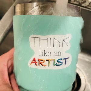 May include: A turquoise stainless steel tumbler with a sticker that says "Think like an artist" in black and rainbow lettering.