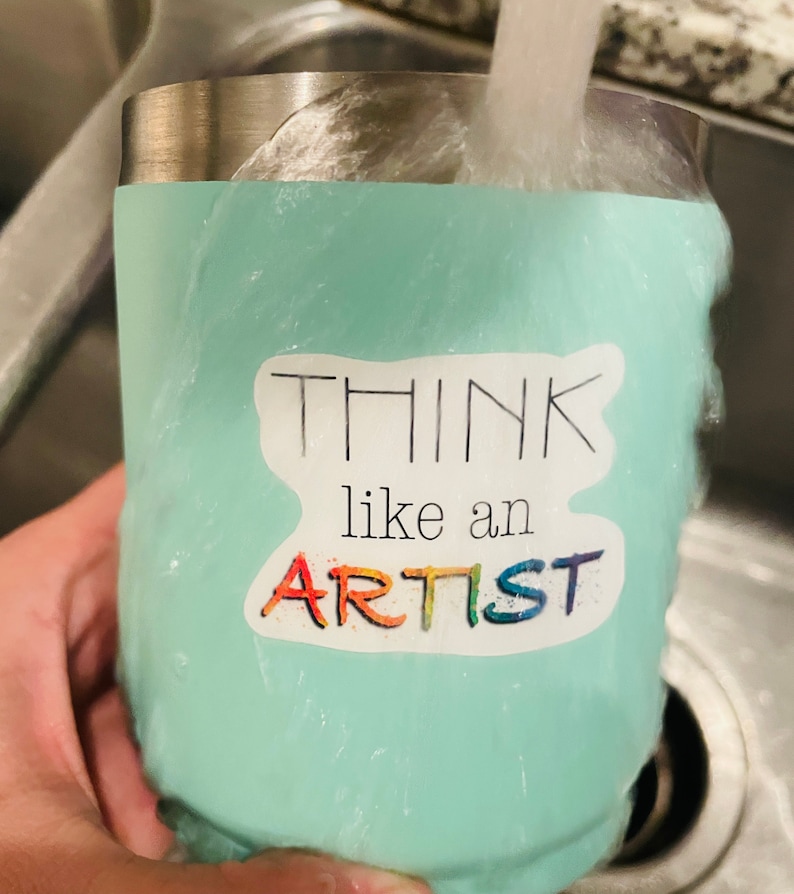 May include: A turquoise stainless steel tumbler with a sticker that says "Think like an artist" in black and rainbow lettering.