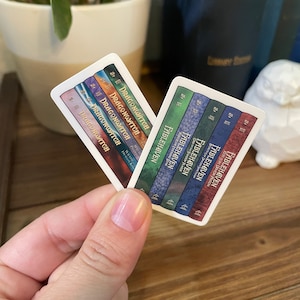 May include: Two sets of book spine stickers, one set featuring the title "Dragonwatch" and the other featuring the title "Fablehaven". The stickers are white with colorful book spines.
