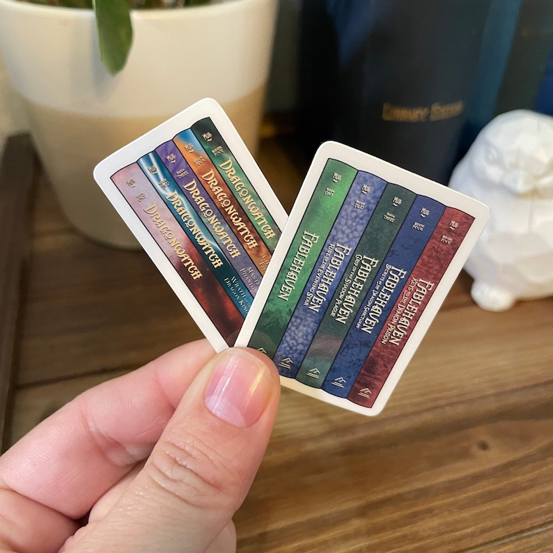 May include: Two sets of book spine stickers, one set featuring the title "Dragonwatch" and the other featuring the title "Fablehaven". The stickers are white with colorful book spines.