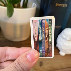 May include: A sticker featuring the covers of five fantasy novels in a series called "Dragonwatch". The books are numbered one through five and each cover features a different dragon with a unique color scheme.