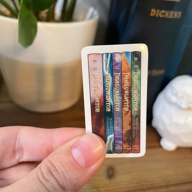 May include: A sticker featuring the covers of five fantasy novels in a series called "Dragonwatch". The books are numbered one through five and each cover features a different dragon with a unique color scheme.